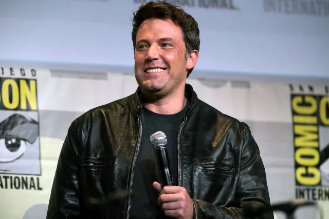 Ben Affleck smiling as he speaks into a microphone on stage at San Diego Comic-Con