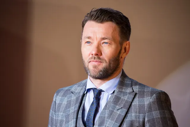 Joel Edgerton in a grey check suit on a red carpet