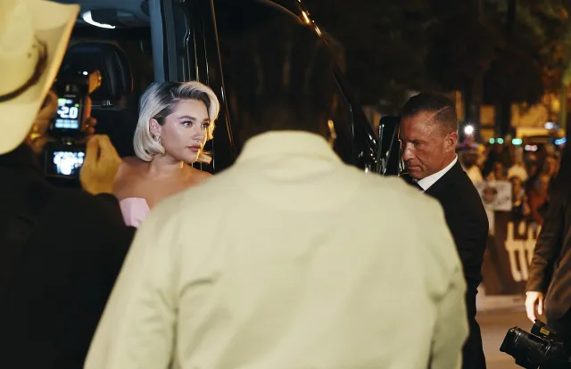 Florence Pugh, with short platinum hair, arriving at an evening premiere surrounded by photographers