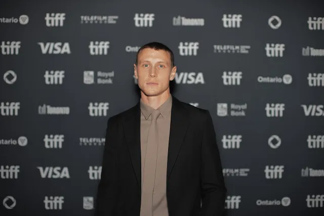 George MacKay in a black suit and taupe shirt and tie on the red carpet at the Toronto International Film Festival