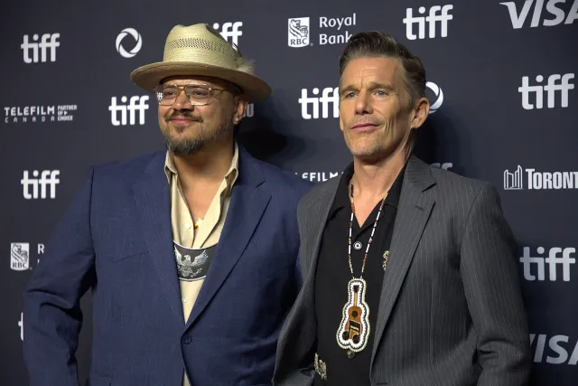 Sterlin Harjo in a straw hat and Ethan Hawke in a pinstripe jacket on the red carpet at the Toronto International Film Festival